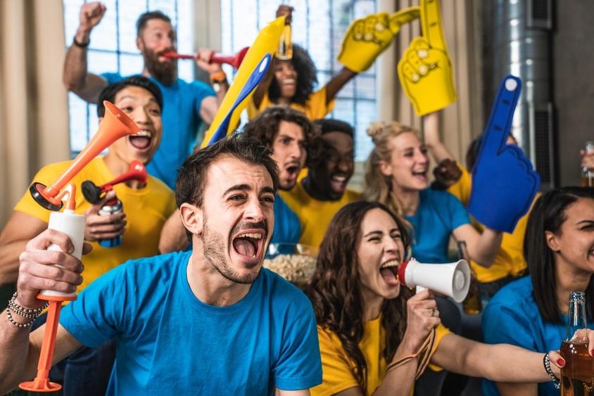 Többnemzetiségű, örömteli sportrajongók nézik otthon a meccset a tévében.