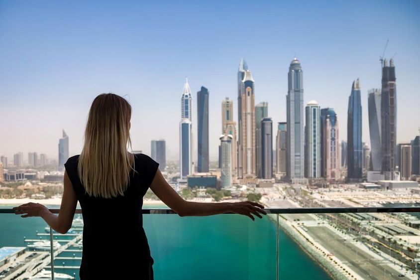 Fekete ruhás nő töprengő tekintettel az erkélyen, kilátással a Dubai, Egyesült Arab Emírségek felhőkarcolóira.