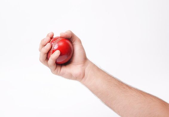 Egy férfi krikettező, aki szilárdan markolja a piros krikett labdát.