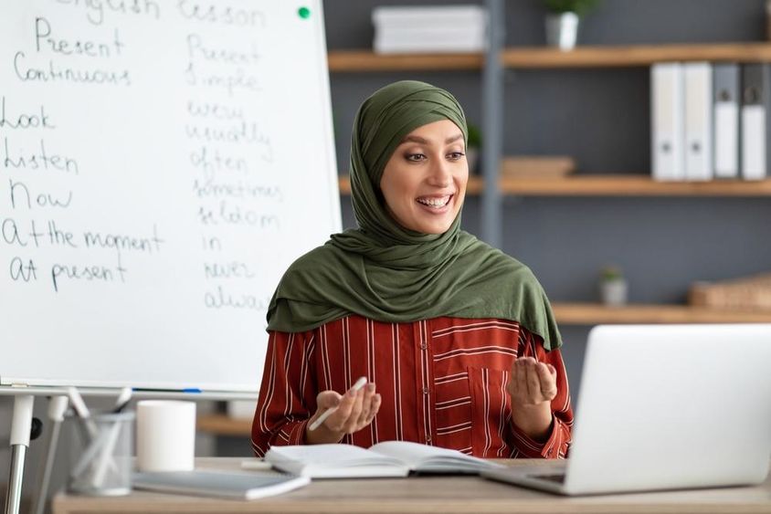 Mosolygós női arab tanár fejkendőben videohívást kezdeményez.