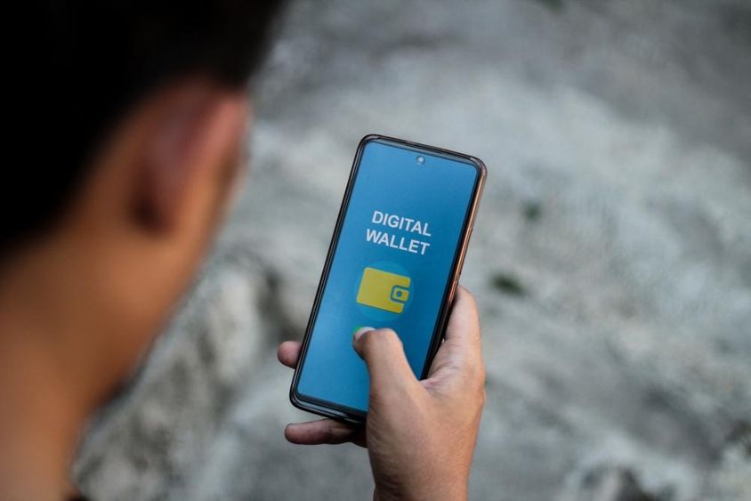 Egy személy keze amely a digitális pénztárca alkalmazások felületét mutatja okostelefon képernyőjén.