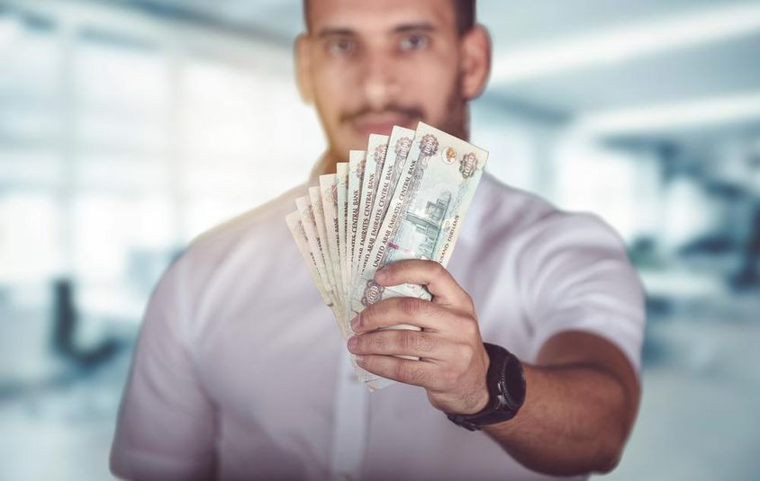Férfi dirham bankjegyekkel a kezében, bankfiók előtt áll.