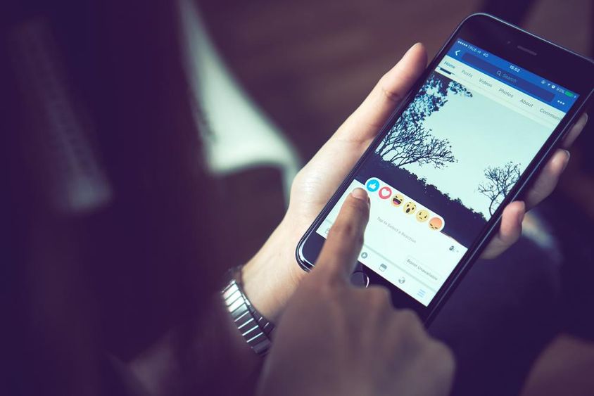 A hand pressing Facebook on an Apple iPhone 6.