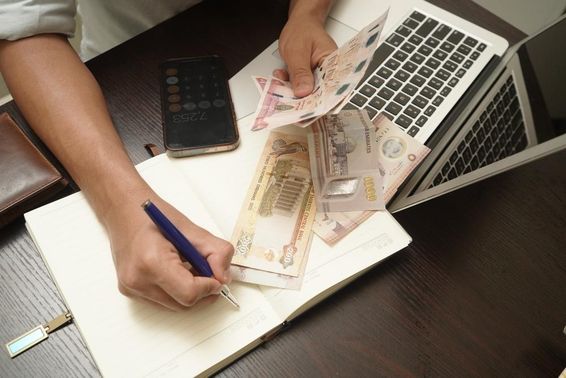 Egy íróasztalnál ülő férfi, aki egy köteg egyesült arab emírségekbeli dirham bankjegyet számol.
