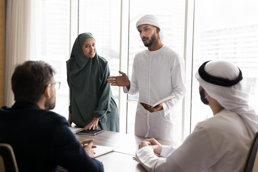 Pár fiatal arab menedzser muszlim ruhában projektet mutat be európai üzleti partnereknek.