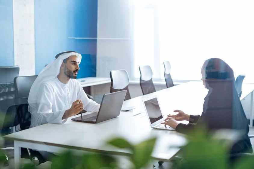 Férfi és nő hagyományos ruhában dolgoznak egy dubai üzleti irodában.
