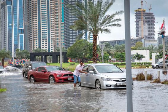 emberek tolnak ki autókat a vízből Dubai elárasztott utcáin.