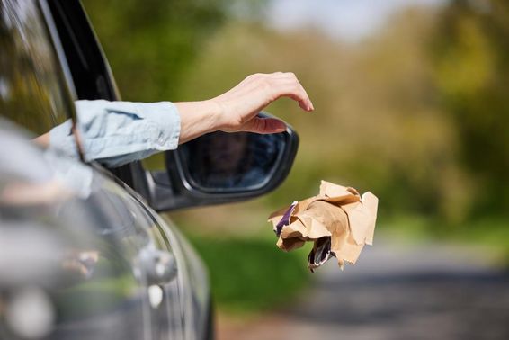 Autóvezető szemetet ejt ki az ablakon az országúton.
