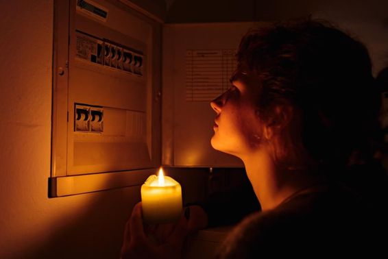 Fiatal nő gyertyákkal teljes sötétségben vizsgálja otthon a biztosítékdobozt.