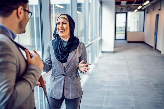 Vonzó mosolygó arab nő ingatlanügynökkel beszélget egy épületről.