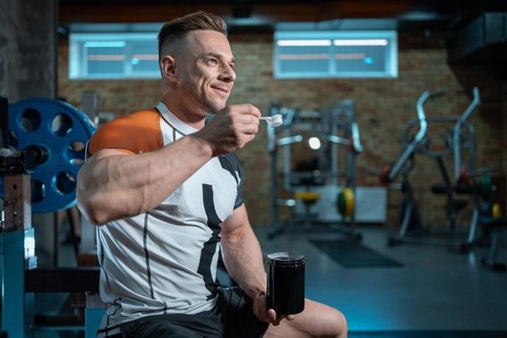 Izmos testépítő sportoló tökéletes testtel, fehérjét tartva az edzőteremben.