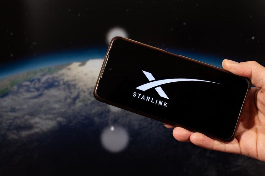 A man's hand holding a smartphone with a Starlink logo in the right hand.