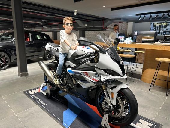Napszemüveget viselő kisfiú egy BMW motorkerékpáron ül.