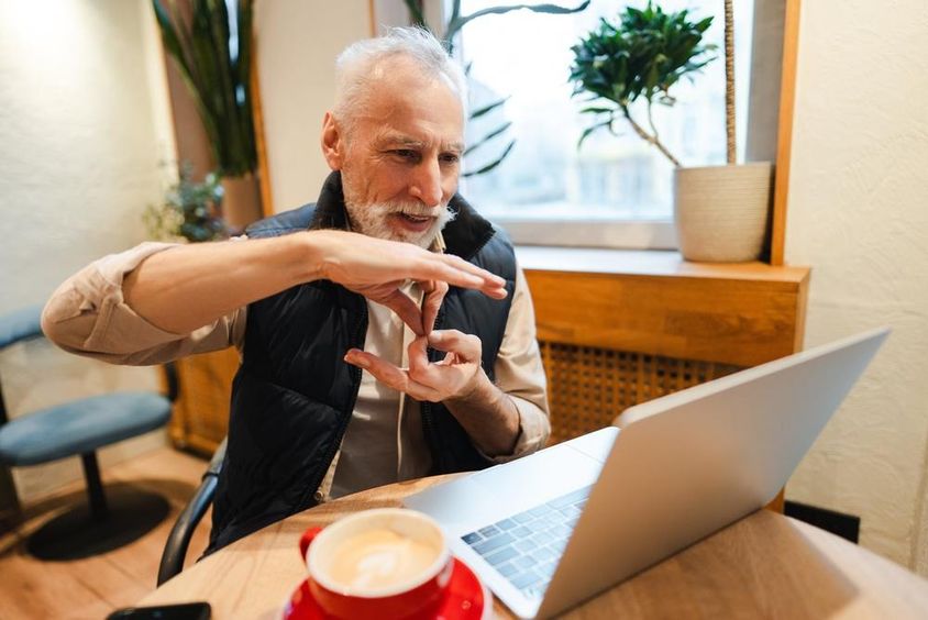 An older bearded man speaking sign language during a video call.