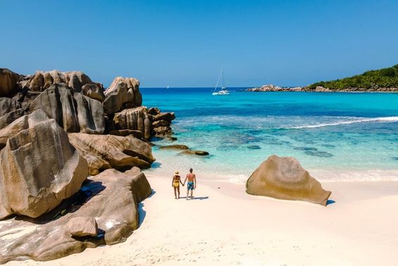 Two travelers walking on the soft white sands of Anse Cocos Beach in Seychelles.