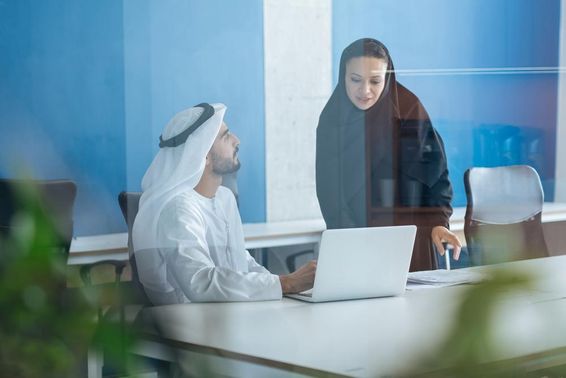 A man and a woman in traditional attire working in a business office in Dubai.