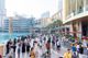 Turisták és helyiek sokszínű tömege sétál a Dubai Mall előtti forgalmas vízparti sétányon.